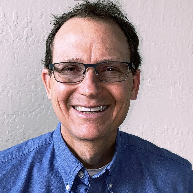Image of Michael Parker, facing the camera with a headshot, shoulders visible. He is smiling, wearing glasses, and dressed in a blue button-up shirt.